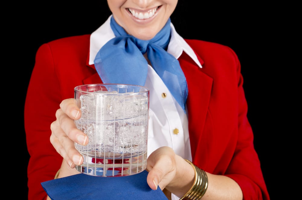 An unidentifiable flight attendant or restaurant server offering a refreshing beverage. Focus on the drink.